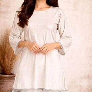 May include: A light beige two-piece outfit. The top has long sleeves with a decorative trim at the cuffs and hem. The outfit is made of a soft, flowing fabric. The logo "SIYABUN" is in the upper right corner.