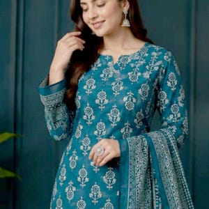May include: Teal-colored printed salwar kameez ensemble. The outfit features a floral pattern in white, long sleeves, and a matching scarf. The design includes a notched neckline and intricate detailing.