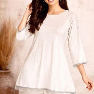 May include: A woman wearing a white tunic and matching pants. The tunic has three-quarter sleeves and a decorative trim. The outfit is simple and elegant, suitable for casual or semi-formal occasions. The brand logo "SIYABUN" is visible in the top right corner.