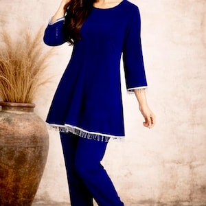 May include: A two-piece, royal blue outfit with a tunic top and pants. The tunic has long sleeves and a flared hemline, both trimmed with white fringe. The pants are a matching blue. The outfit is paired with white heels. The brand logo "SIYABUN" is visible.