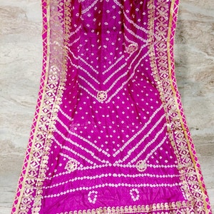 May include: A vibrant magenta textile with a white dotted pattern and gold trim. The fabric features a detailed design with geometric and floral elements. The edges are finished with a gold border and pink trim. The logo "SIYABUN" is visible in the upper right corner.