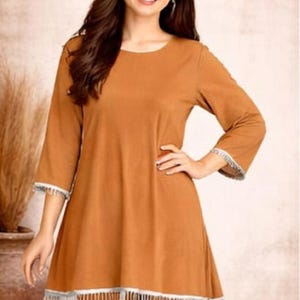 May include: A two-piece outfit in a warm brown hue. The top features three-quarter sleeves and a flared hemline, both trimmed with white fringe. The matching pants complete the ensemble. The brand logo "SIYABUN" is visible in the upper right corner.