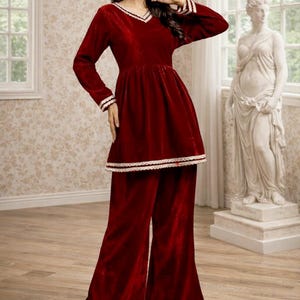Peut inclure: Ensemble deux pièces en velours bordeaux. Le haut à manches longues a un col en V et un ourlet évasé, associé à un pantalon large. Des bordures en dentelle blanche ornent l'ensemble. La modèle porte des sandales dorées.