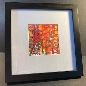 May include: A framed abstract painting with a red, orange, and yellow background. The painting features green and black circles and lines.