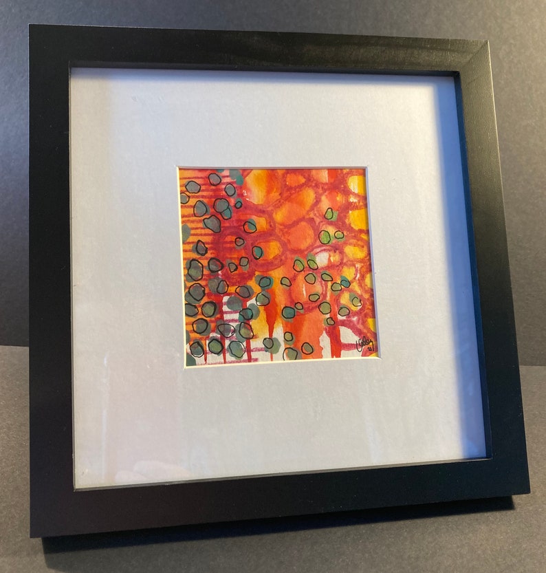 May include: A framed abstract painting with a red, orange, and yellow background. The painting features green and black circles and lines.