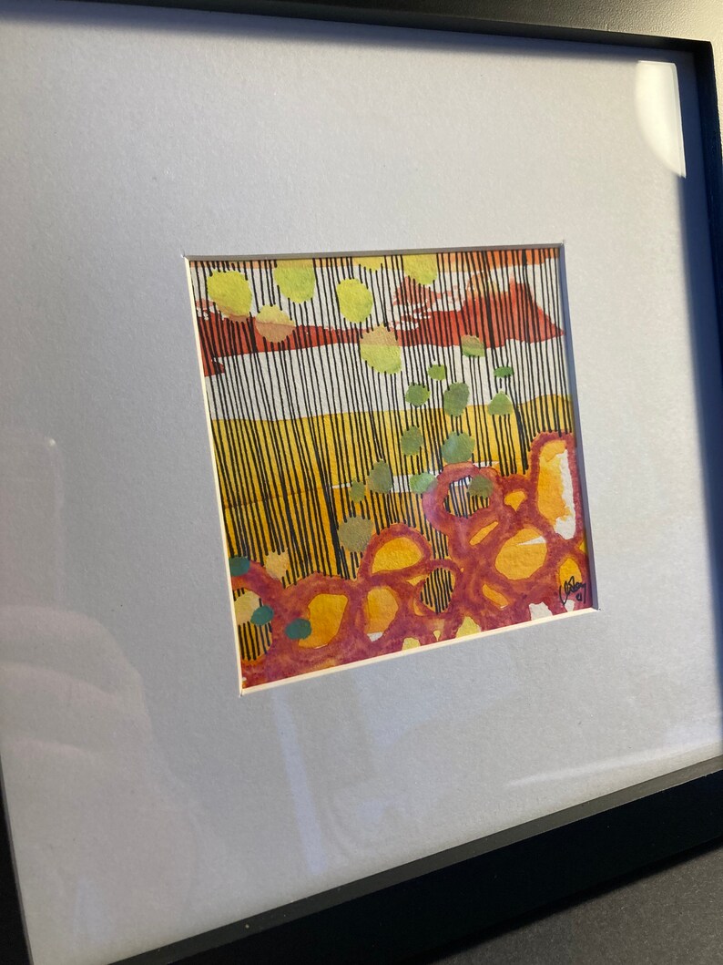 May include: Abstract watercolor painting in a white matted frame. The painting features a mix of yellow, orange, red, and green colors in a geometric pattern.