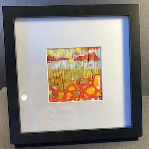 May include: Framed abstract art print with a colorful design featuring red, orange, yellow, green, and black. The print is set against a white background and has a black frame.
