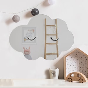 May include: A cloud-shaped wall mirror featuring two silver-colored, curved metal hooks attached directly to the reflective surface. The mirror has a smooth, rounded outline and a clear, polished finish, designed to be mounted on a flat wall surface.