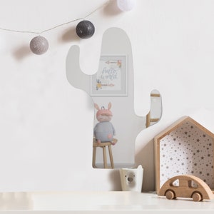 May include: A cactus-shaped wall mirror with a reflective surface. The mirror features a central vertical body with two side arms extending outward. The smooth, curved edges define the silhouette of the plant, providing a clear reflection of the room.