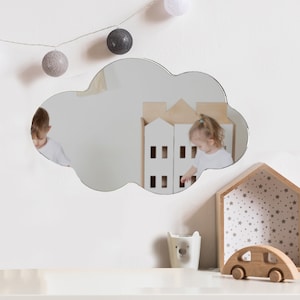 May include: A cloud-shaped wall mirror with a smooth, reflective surface. The mirror features a distinct, rounded, multi-lobed outline that mimics the appearance of a fluffy cloud, providing a clear reflection of the room and objects in front of it.
