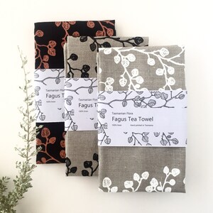 May include: Three linen tea towels with a printed leaf design. The towels are in black, brown, and gray with white leaf designs. The towels are packaged with a label that reads "Tasmanian Flora Fagus Tea Towel 100% linen Hand printed in Tasmania."