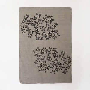 May include: A beige linen tea towel with a black and white floral design. The design features two branches of leaves with small, rounded leaves.