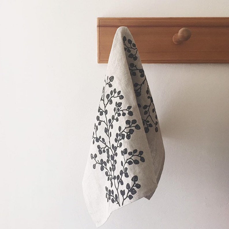 May include: A linen kitchen towel with a black floral print hanging on a wooden hook.