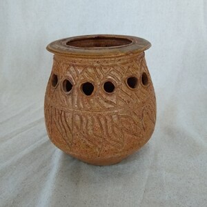 May include: A brown ceramic pot with a textured surface and a row of holes around the middle. The pot has a slightly rounded shape and a wide opening.