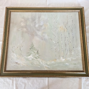 May include: An oil painting of a winter landscape with a light green and white color palette. The artwork features a snow-covered ground, a small evergreen tree, and several birch trees. The painting is framed in a gold and green wooden frame.