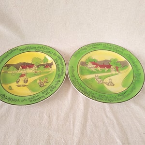 May include: Two vintage ceramic plates with green and yellow borders. The plates feature a countryside scene with a house, trees, and a path. The text on the plates reads: "If we can believe that loving and giving were enoted for improper feeding. It's easier still his fad to be." and "Some of the recipes of Camembert and others of heade de neiltercompan fallsjogasageyser".