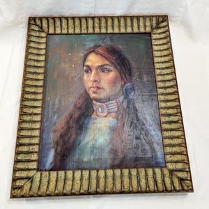 May include: An oil painting portrait of a person with long dark hair, wearing a light blue garment and a multi-layered choker necklace with a central turquoise stone. The artwork is encased in a wide, textured, metallic gold-toned frame.