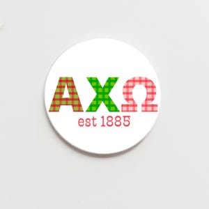 May include: A white round sticker with the letters AXQ in red, green, and pink plaid patterns. The letters are outlined in red. The text "est 1885" is below the letters in red.
