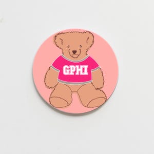 May include: A pink and brown teddy bear wearing a pink shirt with the letters "GPHI" printed in white.