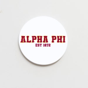 May include: White round coaster with the text "ALPHA PHI EST 1872" in maroon letters with a gold outline.