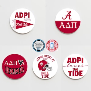 May include: A selection of white and red circular badges with text and graphics. The badges display phrases such as "Roll Tide" and "ADPI", along with a football helmet and the Greek letters ΑΔΠ. The badges are officially licensed products.