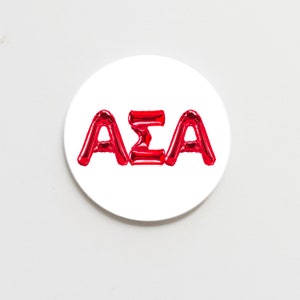 May include: A white round sticker with the letters "AΣA" in red balloon letters.