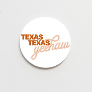 May include: White round coaster with the words "TEXAS TEXAS yeehaw" in orange and peach-colored rope-style lettering. The coaster is a simple, yet stylish accessory.