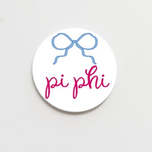 May include: White round coaster with a blue bow and the text "pi phi" in pink.