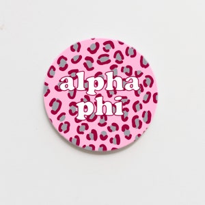 May include: Pink and grey leopard print circle sticker with the text "alpha phi" in white.