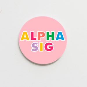 May include: A pink round sticker with the text "ALPHA SIG" in rainbow colors.