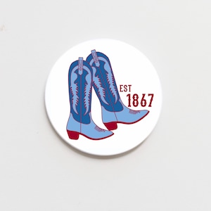 May include: A white round coaster with a blue and red illustration of two cowboy boots. The text "EST 1867" is printed in red.