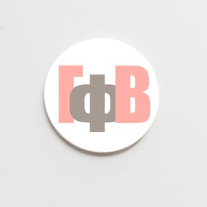 May include: A white round coaster with the Greek letters Gamma, Phi, and Beta in pink and gray. The letters are stacked on top of each other, with the Phi in the center.
