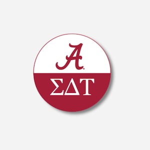 May include: A circular badge divided horizontally, with a white upper section and a maroon lower section. The upper section displays a maroon script letter "A". The lower section features the Greek letters "ΣΔΤ" in white.