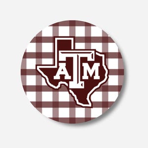 May include: A circular sticker featuring a maroon and white gingham plaid pattern background. Centered on the sticker is a maroon silhouette of the state of Texas with a white outline, containing the white collegiate-style letters ATM.