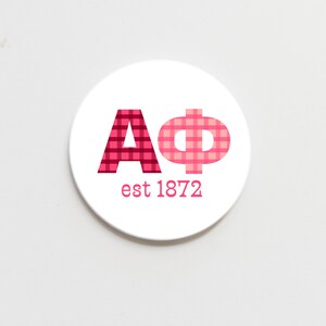 May include: A white circle with a red and pink checkered "AΦ" and the text "est 1872" in black.