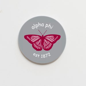 May include: A grey circle sticker with a pink butterfly and the text "alpha phi est 1872".