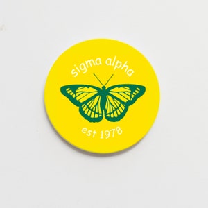 May include: A yellow circle sticker with the text "sigma alpha est 1978" in white. A green butterfly is in the center of the circle.
