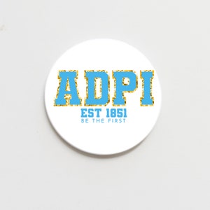 May include: A white round sticker with gold glitter lettering that reads "ADPI EST 1851 BE THE FIRST" in blue lettering.