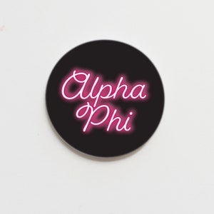 May include: A black circle sticker with the text "Alpha Phi" in pink neon lettering.