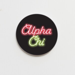 May include: A black circle sticker with the words "Alpha Chi" in neon pink and green lettering.