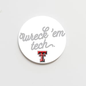 May include: A white, circular item with the text "wreck 'em tech" in a rope-like font. The Texas Tech logo, a red "T" inside a black square, is at the bottom. The item is likely a decorative item or accessory.
