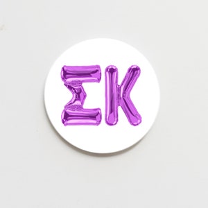 May include: Purple balloon letters spelling out "ΣΚ" on a white background.