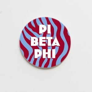 May include: A round button with a blue and red zebra stripe pattern. The text "Pi Beta Phi" is written in white letters on the button.