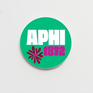 May include: A circular, green sticker featuring the white letters "APHI" and the magenta numbers "1812". A magenta floral design is on the lower left. The sticker is set against a white backdrop.