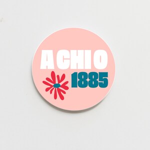 May include: A pink circle sticker with the text "A Chi O 1885" in white and blue lettering. A red stylized flower is to the left of the year.