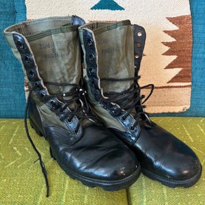 May include: A pair of black leather boots with green canvas uppers. The boots have laces and are worn. The text "10% PROTECT" is visible on the canvas.