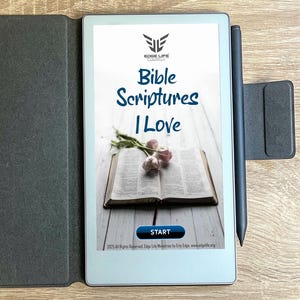 Puede incluir: Un lector electrónico con el texto "Bible Scriptures I Love" en la pantalla. La pantalla muestra un libro abierto con flores. Un lápiz óptico negro y una funda negra también son visibles.