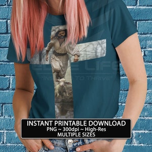 Puede incluir: Una camiseta azul turquesa con un gráfico de un hombre corriendo con un cordero. El gráfico tiene la forma de una cruz. El texto "E LIFE" y "INS TO THRIVE" está impreso en la camiseta.