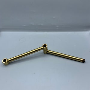 May include: A gold metal pipe fitting with two angled sections.