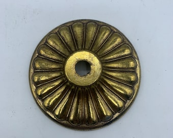 May include: A gold-toned metal decorative accent with a scalloped edge and a central hole. The accent has a sunburst design.
